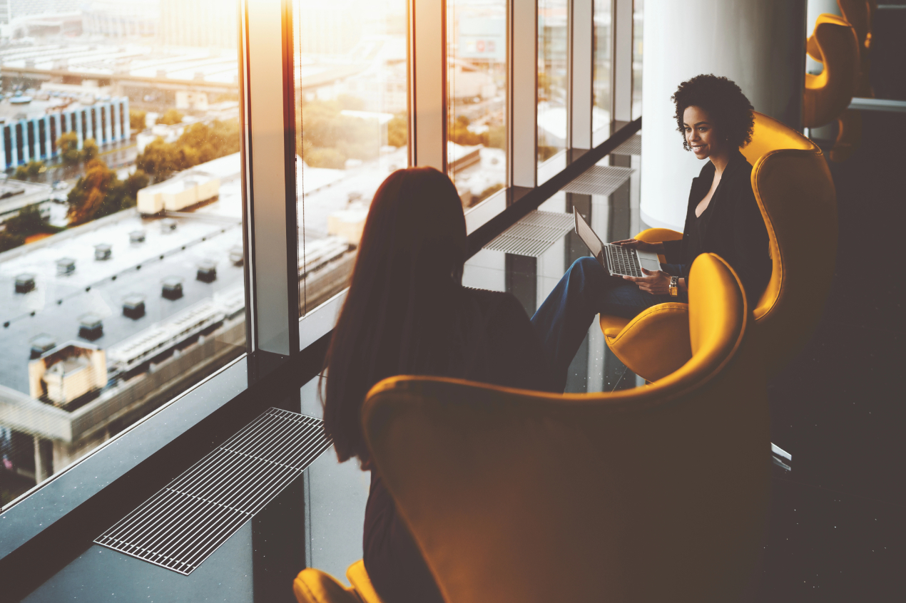 Two businesswomen having work meeting near office windows Two businesswomen having work meeting near office windows