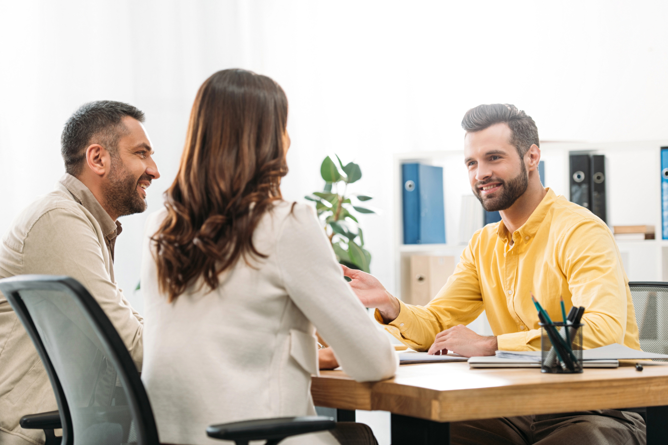 Advisor sitting at table and smiling to man and woman in office Advisor sitting at table and smiling to man and woman in office