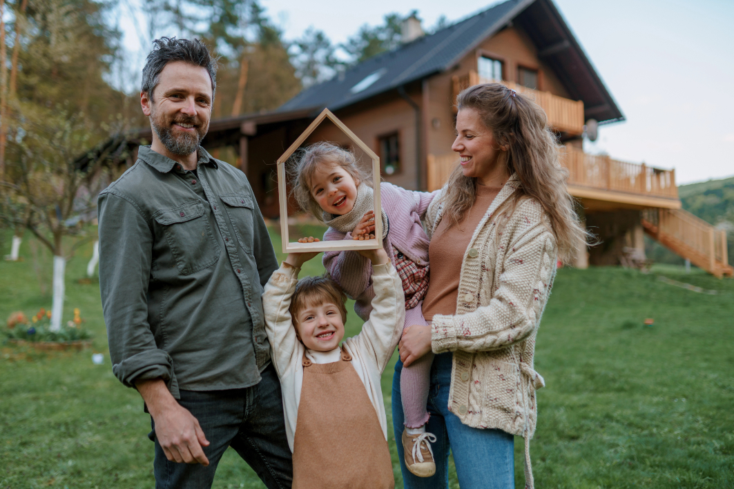 Happy family is standing near their modern house, smiling and looking at camera Happy family is standing near their modern house, smiling and looking at camera